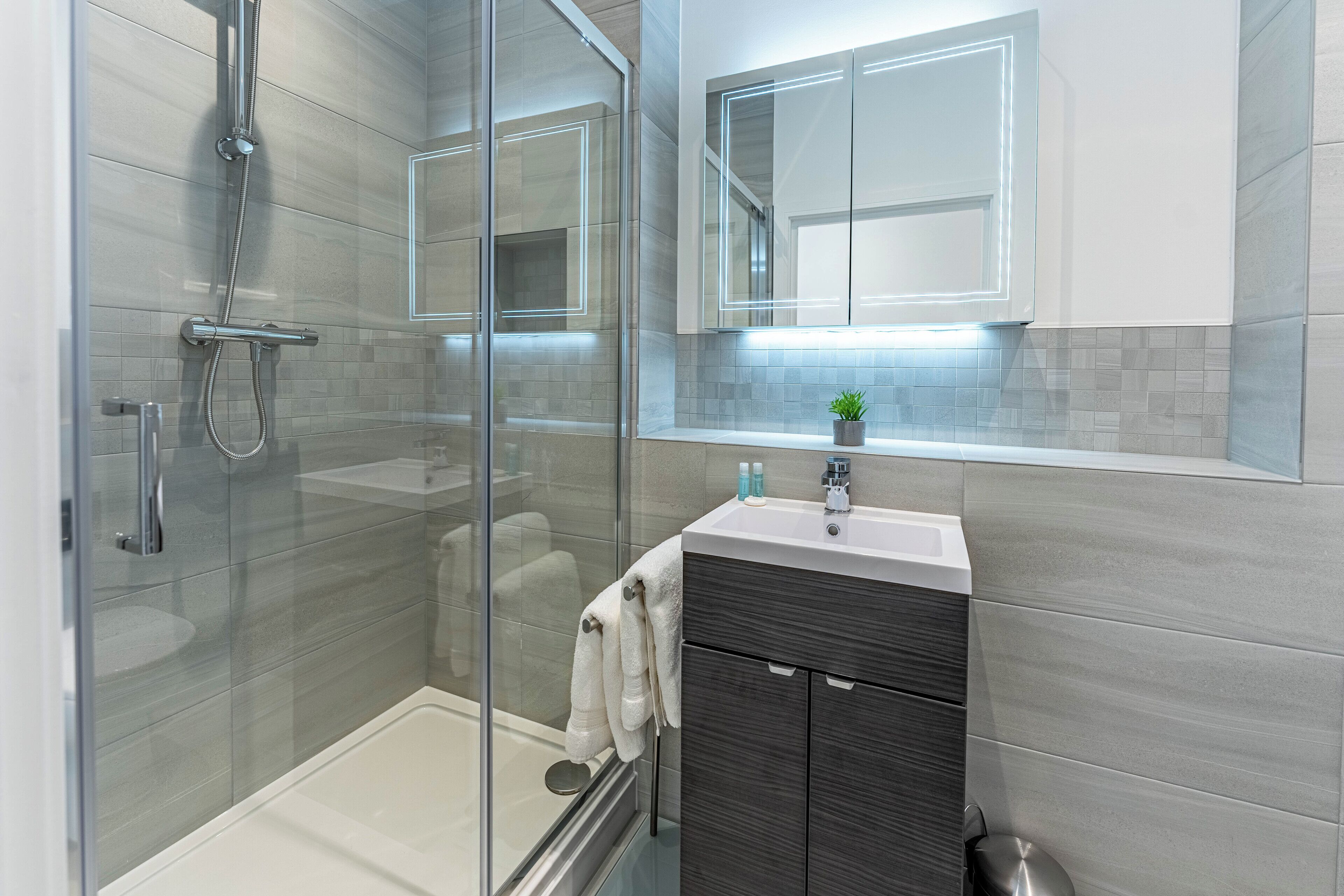 A modern bathroom with a glass shower enclosure, a white bathtub, and a vanity with dark wood cabinetry.