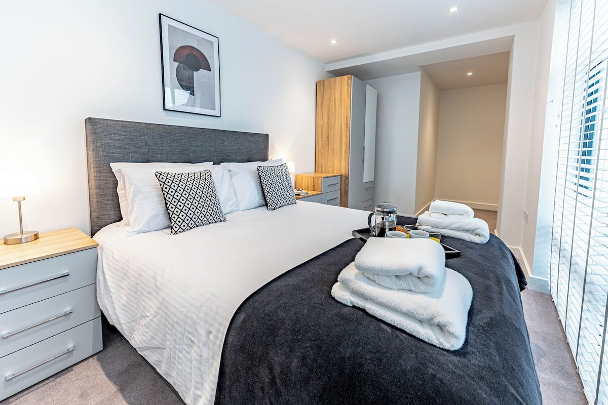 Habitación de hotel moderna con una cama grande, una mesita de noche, un armario y un baño visible a través de una puerta abierta.