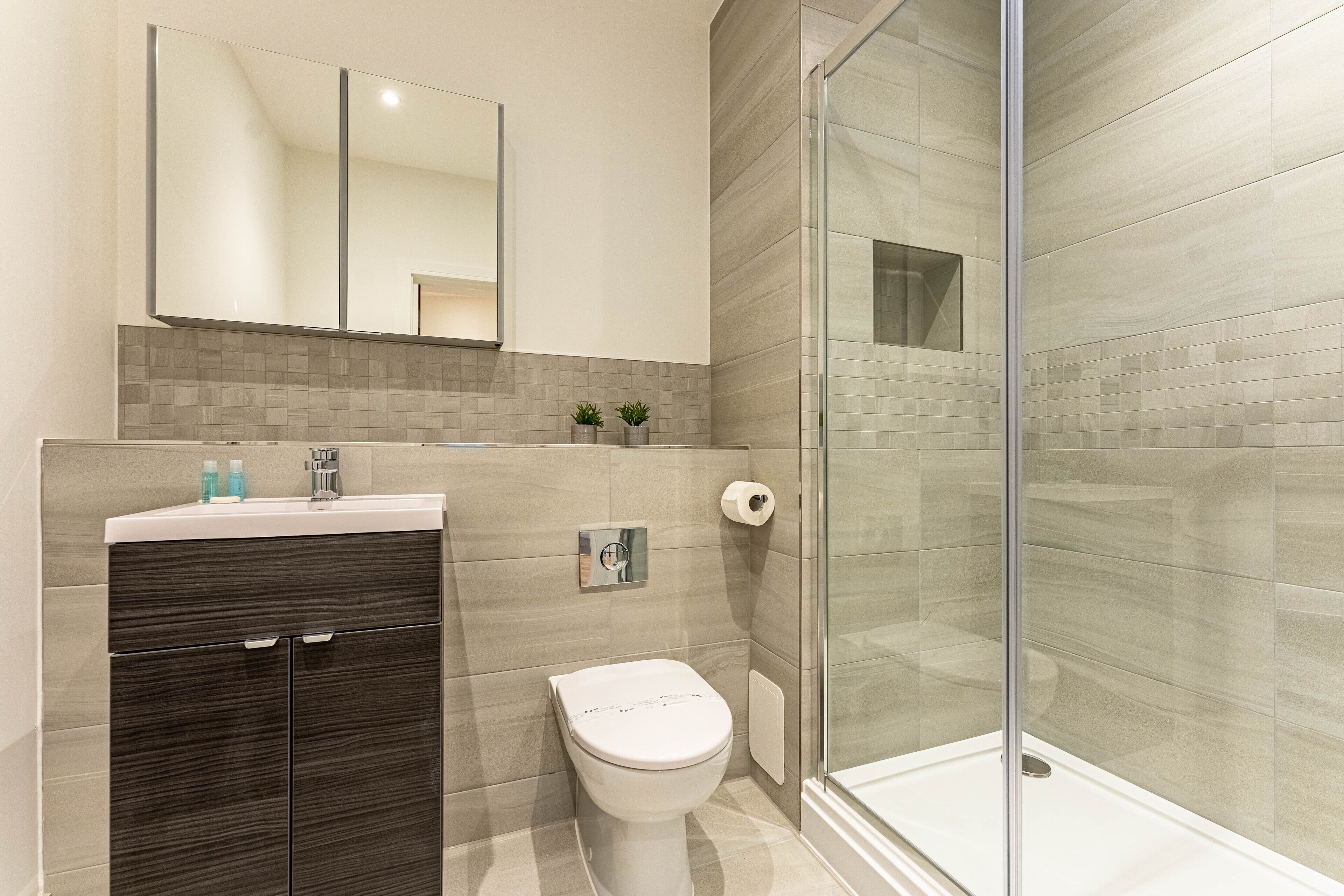 A modern bathroom with a glass shower enclosure, a dark wood vanity, and a white toilet.