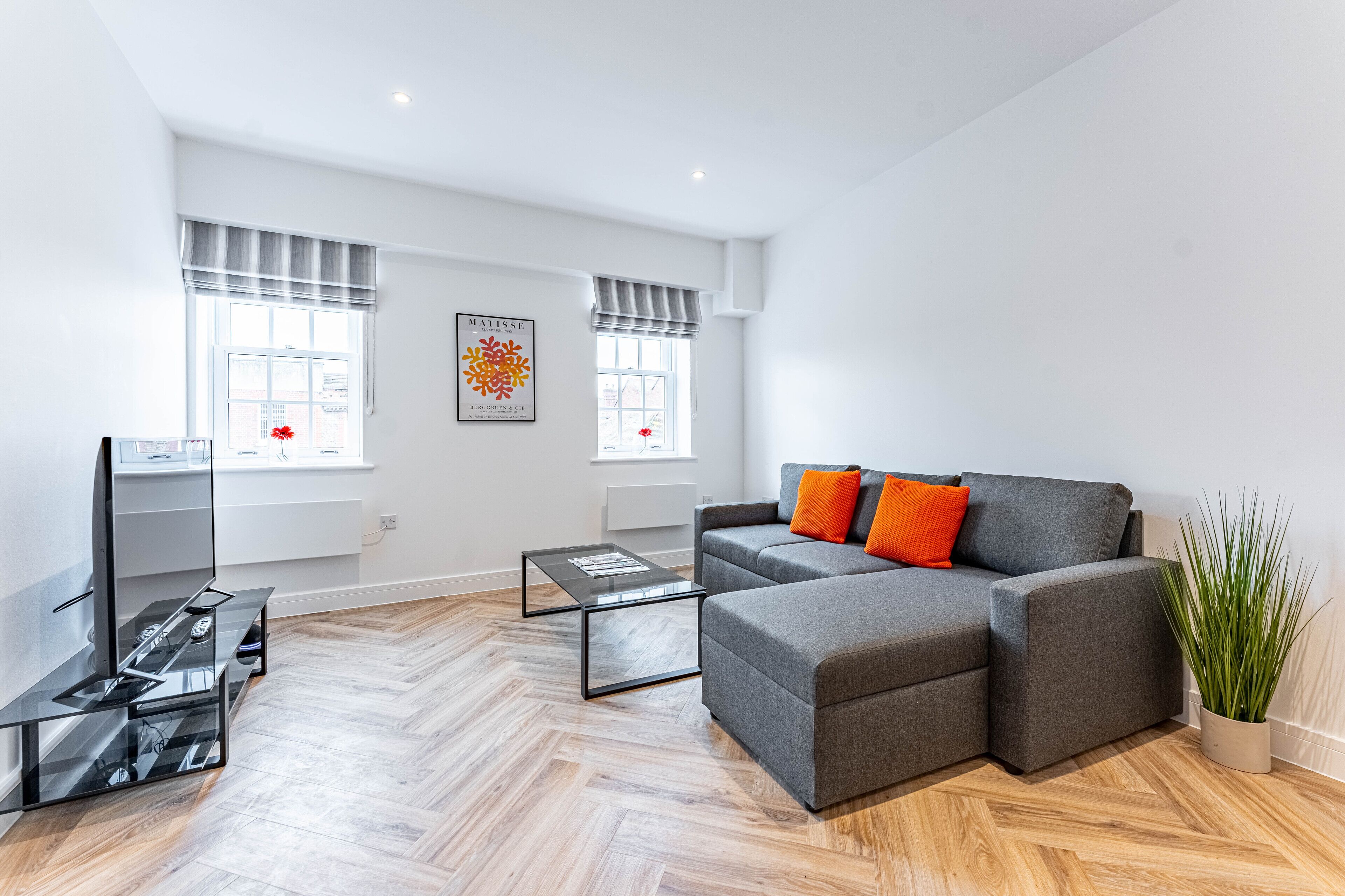 Ein modernes Wohnzimmer mit einem grauen Ecksofa, einem Glastisch und einer Topfpflanze.