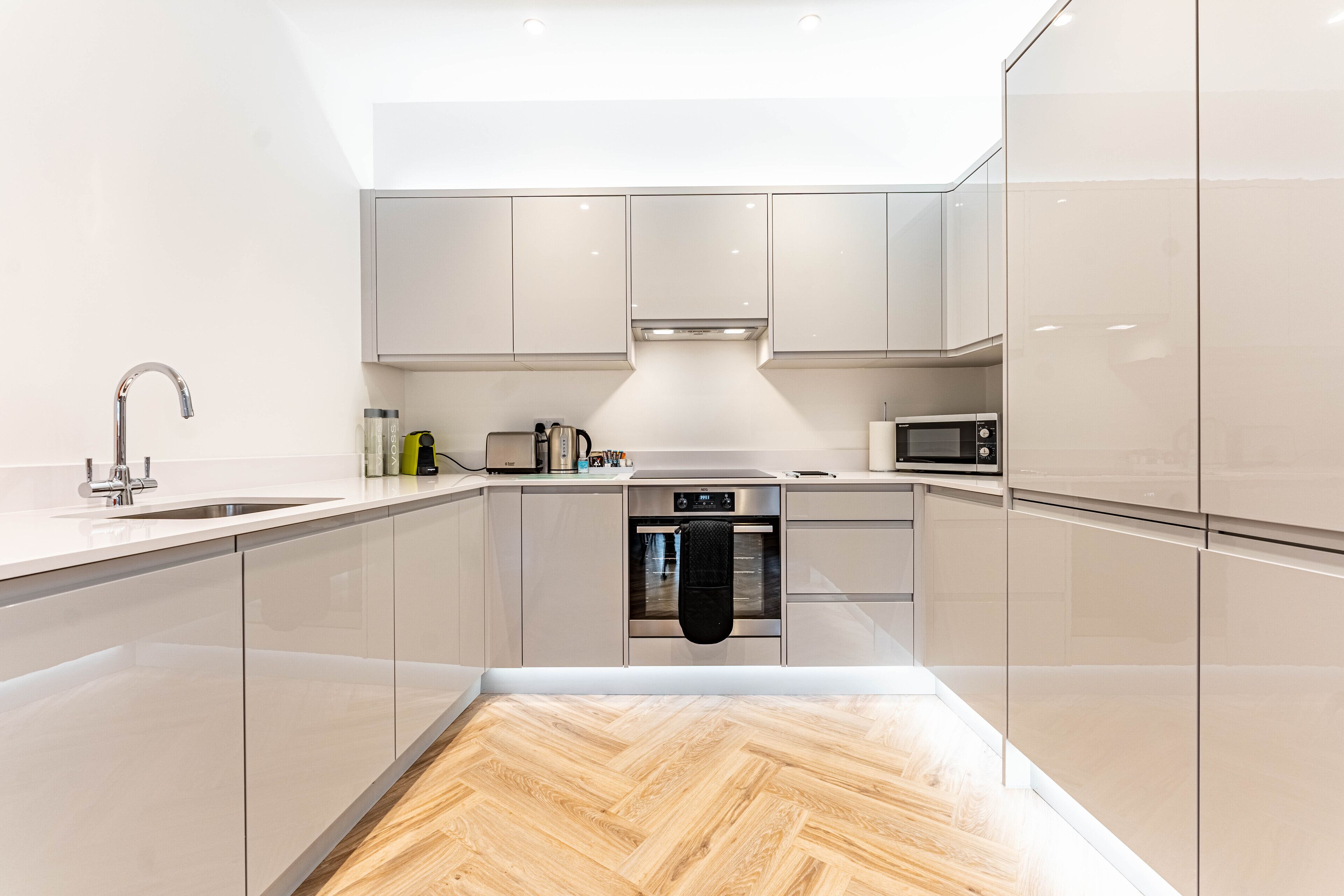 Une cuisine moderne avec un parquet en bois disposé en chevrons, des appareils en acier inoxydable et des meubles de couleur claire.