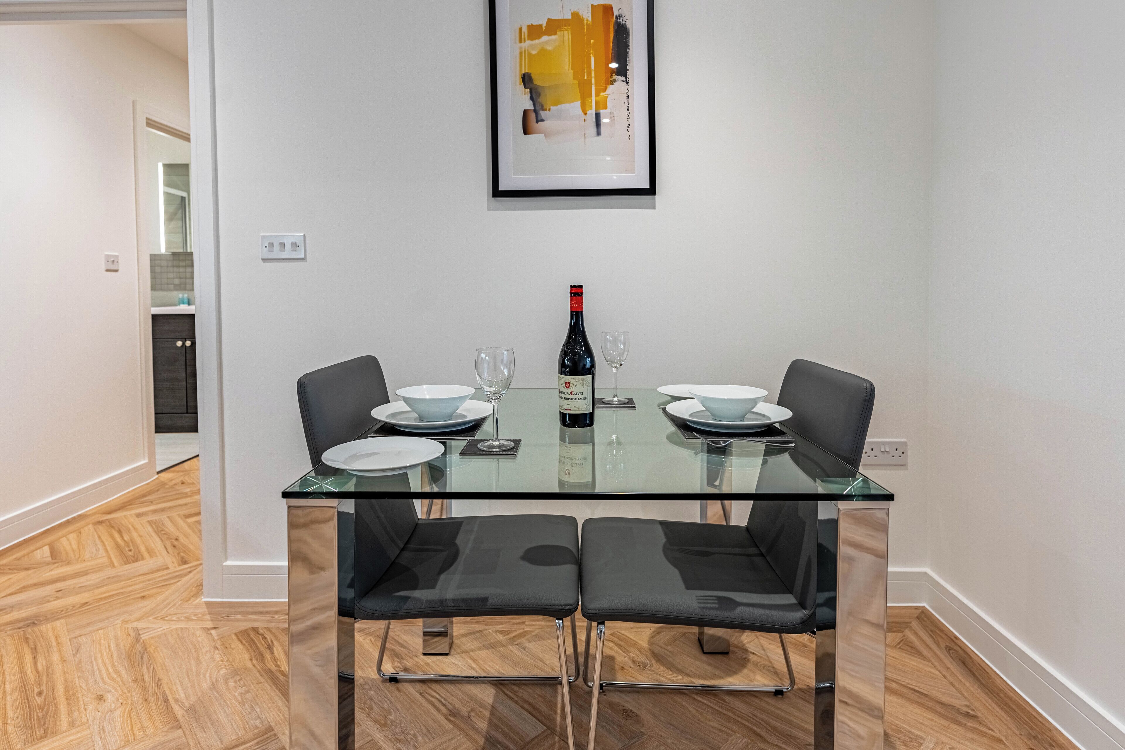 A dining area with a glass table, four black chairs, and a bottle of wine.