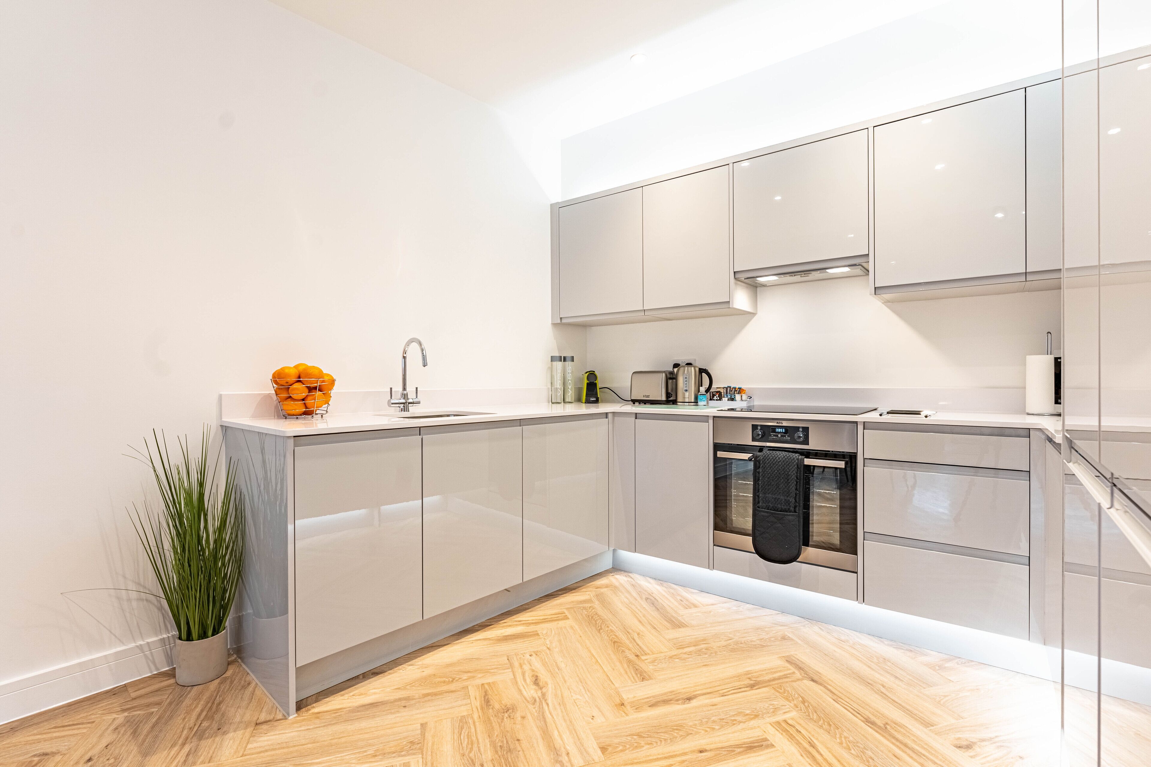 A modern kitchen with a herringbone wood floor, white cabinetry, and stainless steel appliances.