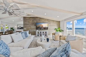 Uma sala de estar moderna com uma TV grande, assentos confortáveis, uma parede de destaque em pedra e vista para o oceano.
