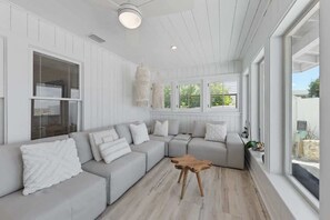 A modern living room with a sectional sofa, a wooden coffee table, and a large window offering a view of the outdoors. - Serendipity Gulfront | Hot Tub | Heated Pool | Golf Cart (Anna Maria)