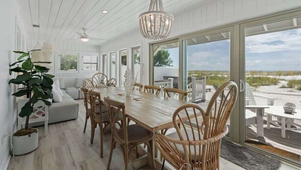 Un comedor con una mesa y sillas de madera, una araña y ventanas amplias con vista a la playa.