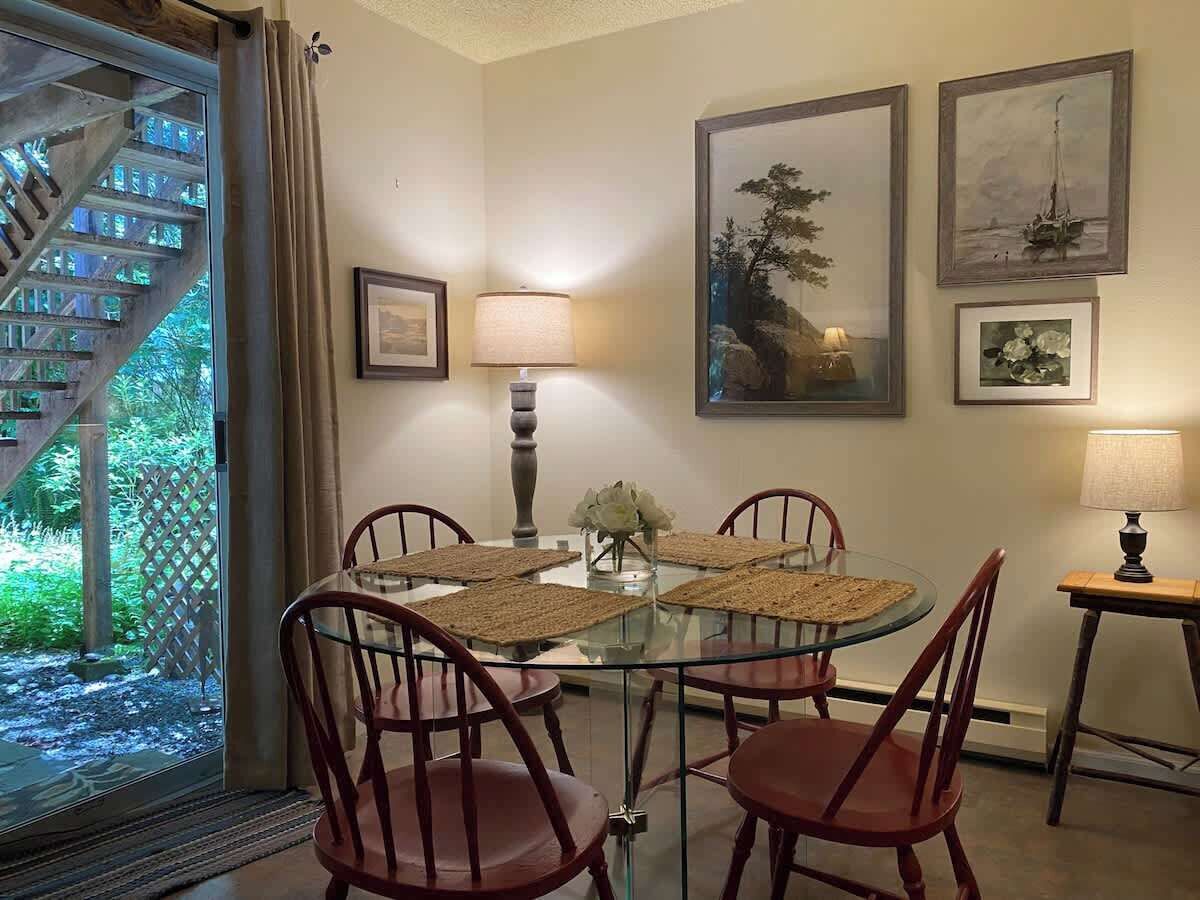Un comedor con mesa de vidrio, cuatro sillas, dos lámparas de pared y cuadros enmarcados.