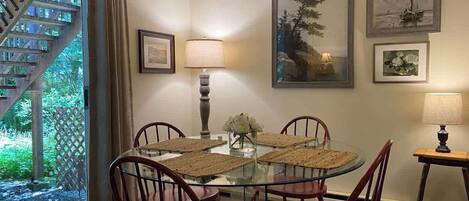 Un comedor con mesa de vidrio, cuatro sillas, dos lámparas de pared y cuadros enmarcados.