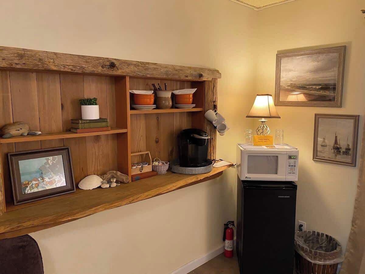 A kitchenette with a microwave, coffee maker, and shelves with dishes and a framed picture.