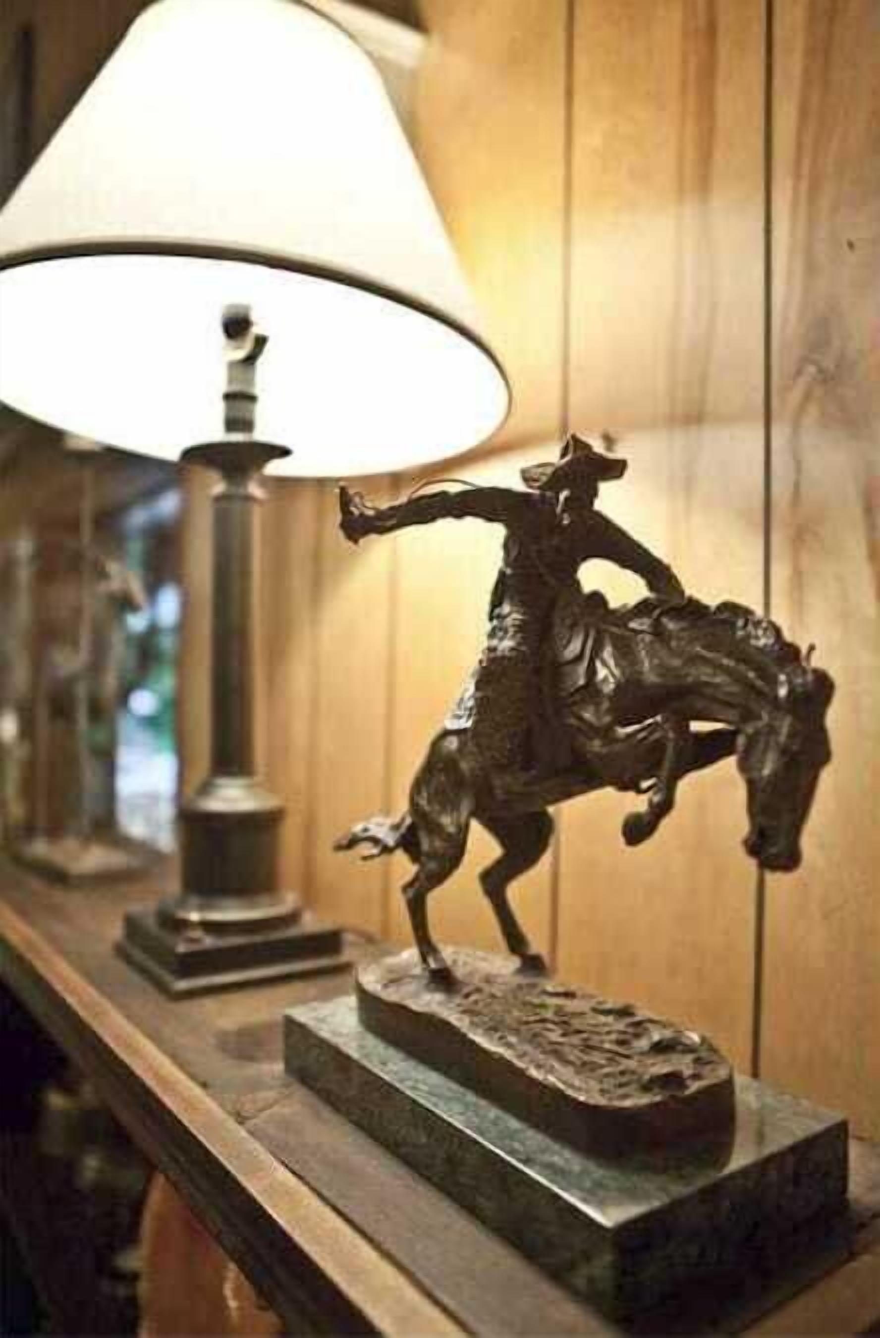 A bronze statue of a horse and rider on a rectangular base, placed on a wooden surface with a lamp in the background.