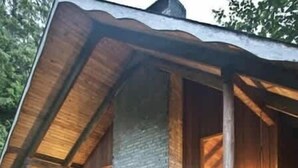 Un rustico chalet con parete in pietra, travi in legno e portico coperto con sedie.