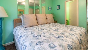 Un dormitorio con una colcha estampada con motivos florales, un cabecero de madera y un espejo en la pared.