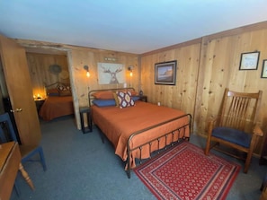 A cozy room with a bed, a chair, a desk, and a door leading to another room.