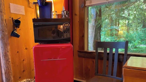Una cocina compacta con un refrigerador rojo, un microondas y una silla de madera.