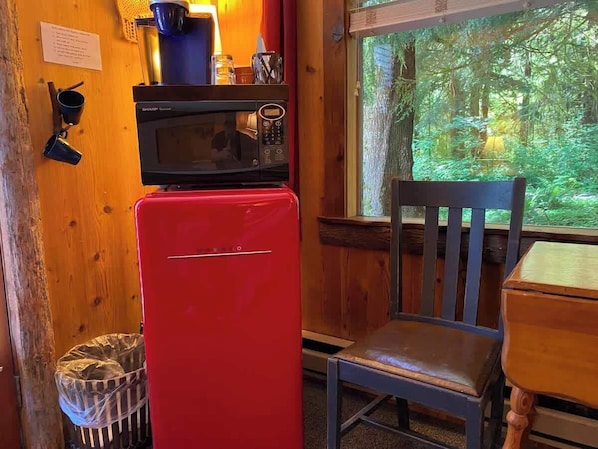 A compact kitchen with a red refrigerator, a microwave, and a wooden chair.
