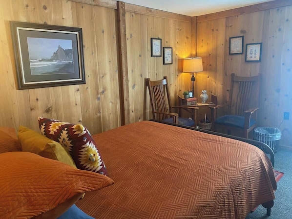 A hotel room with a large bed, a chair, a small table, and a lamp.