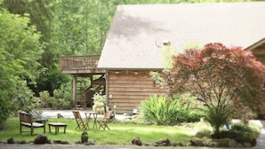 A wooden cabin with a porch, surrounded by a well-maintained garden with various plants and a small table and chairs. - Lady Lodge Room near Olympic National Park (Forks)
