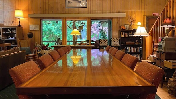 A large wooden conference table surrounded by cushioned chairs in a room with wooden walls and large windows. - Lady Lodge Room near Olympic National Park (Forks)