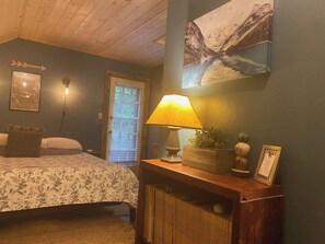 Un dormitorio con cama, una mesita de noche con lámpara, un cuadro enmarco y una ventana con persianas.