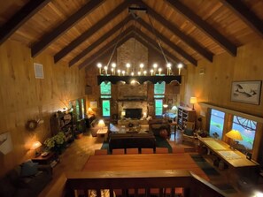 A spacious living room with a high ceiling, wooden beams, a fireplace, and a cozy seating area.