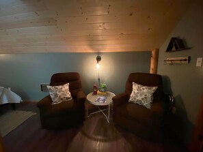 Een gezellige kamer met twee bruine fauteuils, een klein rond tafeltje met een lamp en een houten plafond.