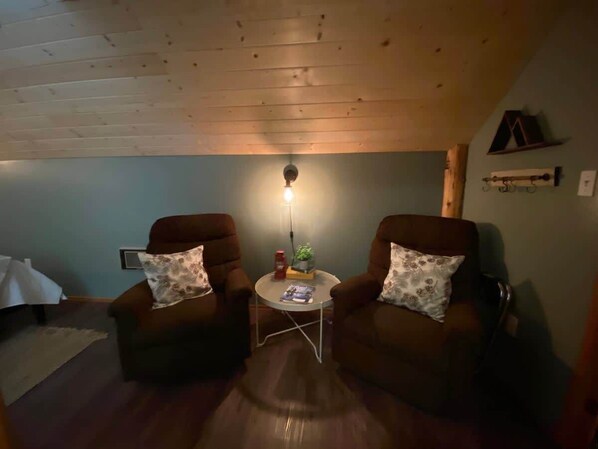 A cozy room with two brown armchairs, a small round table with a lamp, and a wooden ceiling.