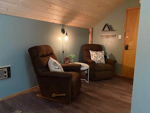 Una habitación acogedora con dos sillones reclinables marrones, una mesita con una planta y una lámpara fijada a la pared.