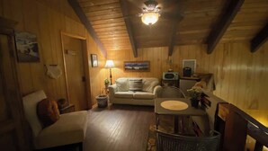A cozy cabin interior with a wooden ceiling, a sofa, a dining table, and a television.