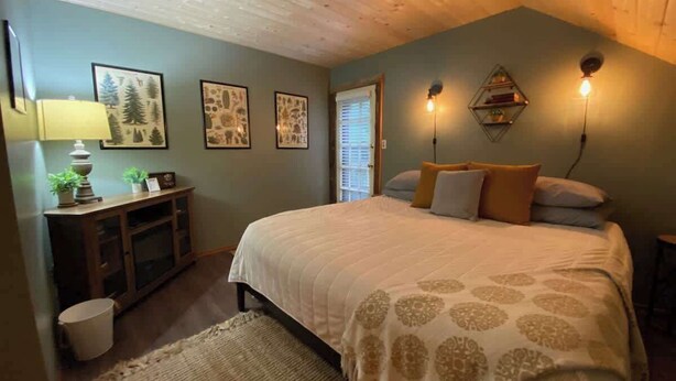 A bedroom with a bed, a desk, a lamp, and framed pictures on the wall.