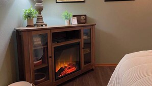 A room with a wooden cabinet containing a fireplace, a lamp, and framed botanical prints on the wall. - Lily Lodge Room near Olympic National Park (Forks)