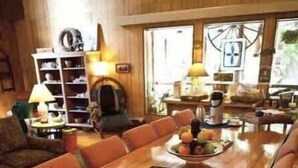 A wooden dining table with a placemat and a fruit bowl in the center, surrounded by orange upholstered chairs. - Lily Lodge Room near Olympic National Park (Forks)