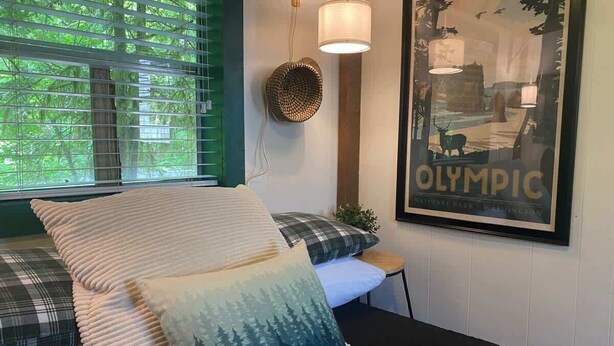 A bedroom with a bed, pillows, a wall-mounted lamp, and a framed picture of the Olympic National Park. - Outback Rustic Cabin near Olympic National Park (Forks)