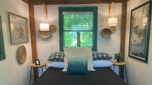 A neatly arranged bedroom with a large bed, two bedside tables, a window with blinds, and wall-mounted lamps.