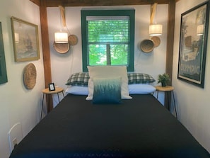 Une chambre à coucher bien aménagée, avec un grand lit, deux tables de chevet, une fenêtre avec des stores et des lampes fixées au mur.