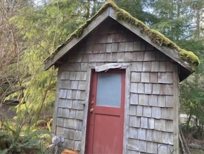 Une petite cabane en bois avec une porte rouge, entourée d’arbres.