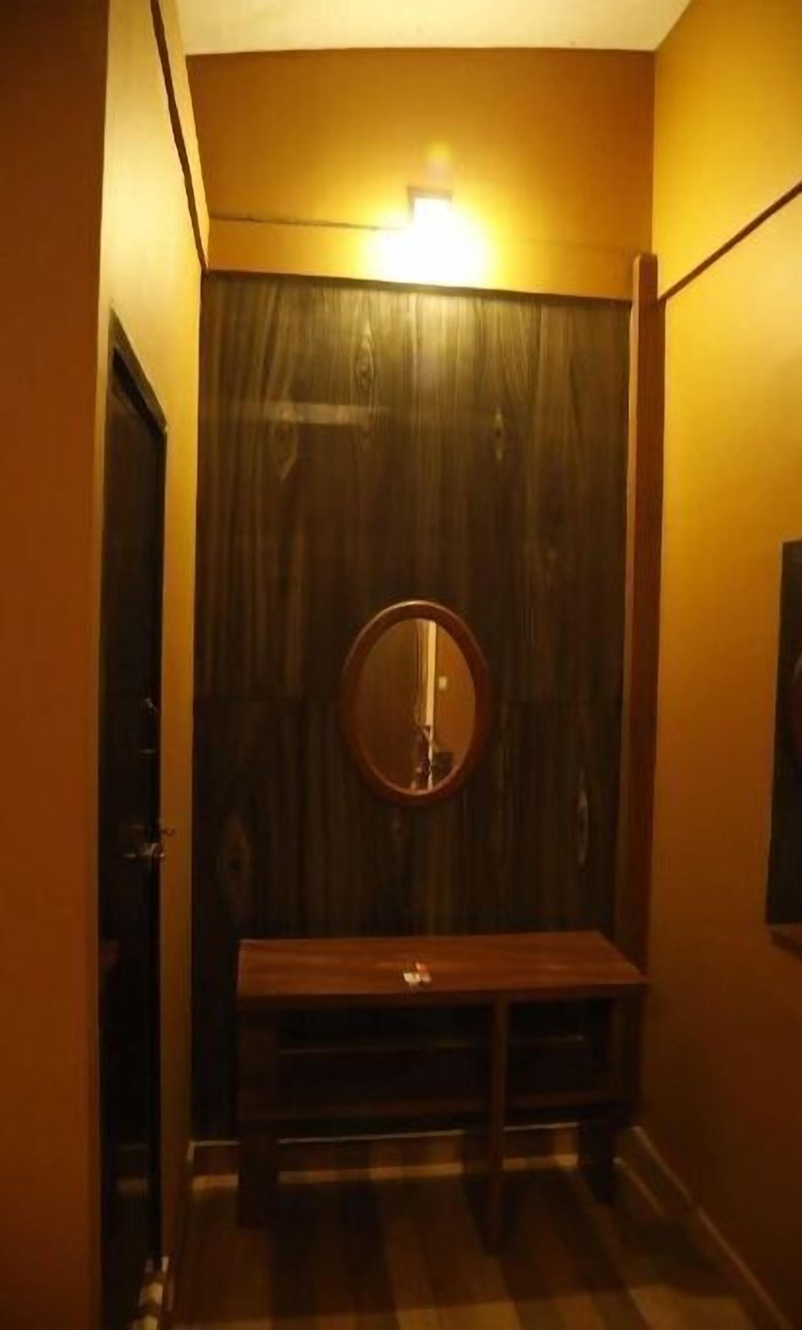 A small, dimly lit room with a wooden bench, a round mirror on the wall, and a door to the left.