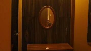 A small, dimly lit room with a wooden bench, a round mirror on the wall, and a door to the left.