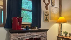 Een open haard met een stenen gevel, een koffiezetapparaat en een lamp op een houten tafel ernaast.