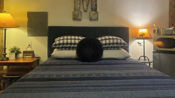Slaapkamer met een groot bed, twee bedlampen, een wandtelevisie en een grote decoratie in de vorm van een 'M'.