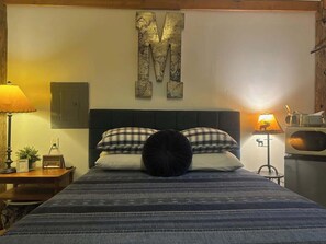 Slaapkamer met een groot bed, twee bedlampen, een wandtelevisie en een grote decoratie in de vorm van een 'M'.