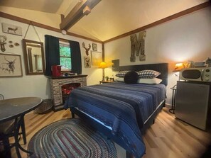 A cozy bedroom with a bed, a small table, a fireplace, and a refrigerator. - Outback Too Rustic Cabin by Olympic National Park (Forks)