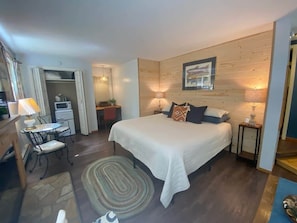 Een slaapkamer met een groot bed, een bureau met lamp, een stoel, een magnetron en een kledingkast.
