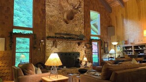A cozy living room with a stone wall, a mounted deer head, a fireplace, and a large window.