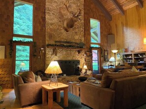 A cozy living room with a stone wall, a mounted deer head, a fireplace, and a large window. - Sacagawea Lodge Room near Olympic National Park (Forks)