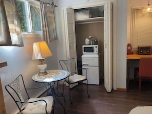 Een knus ingerichte kamer met een eettafel, stoelen, een lamp, een magnetron en een kast met een kat.