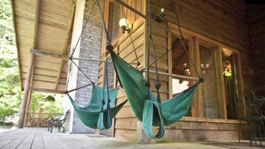 A wooden building with a porch, two green hammocks hanging from the ceiling, and a brick wall.