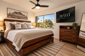 A bedroom with a bed, a ceiling fan, a TV, a nightstand, a dresser, and a window with a view of trees.