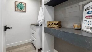 Un baño moderno con un tocador blanco, una cesta, un cuadro enmarcado y una toalla colgada en la pared.
