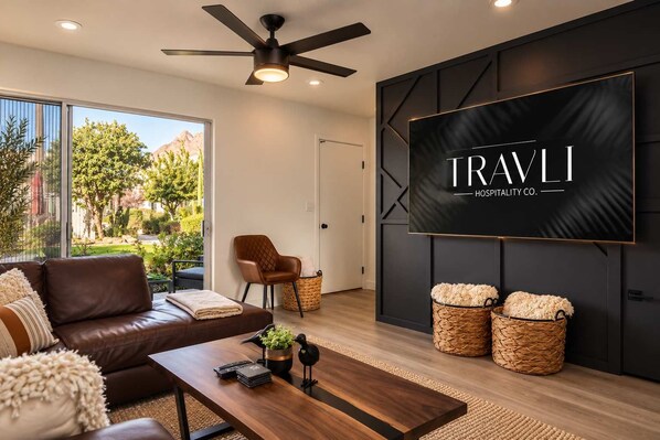 A modern living room with a leather sofa, a coffee table, a TV mounted on the wall, and a view of the outdoors.