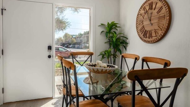 Un comedor con una mesa de vidrio, cuatro sillas de madera y un reloj de madera grande en la pared.